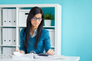 57152361 - young businesswoman with glasses calculates tax at desk in office